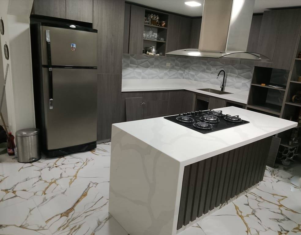 Isla de cocina en cuarzo blanco con cascada, estufa empotrada y piso marmolado