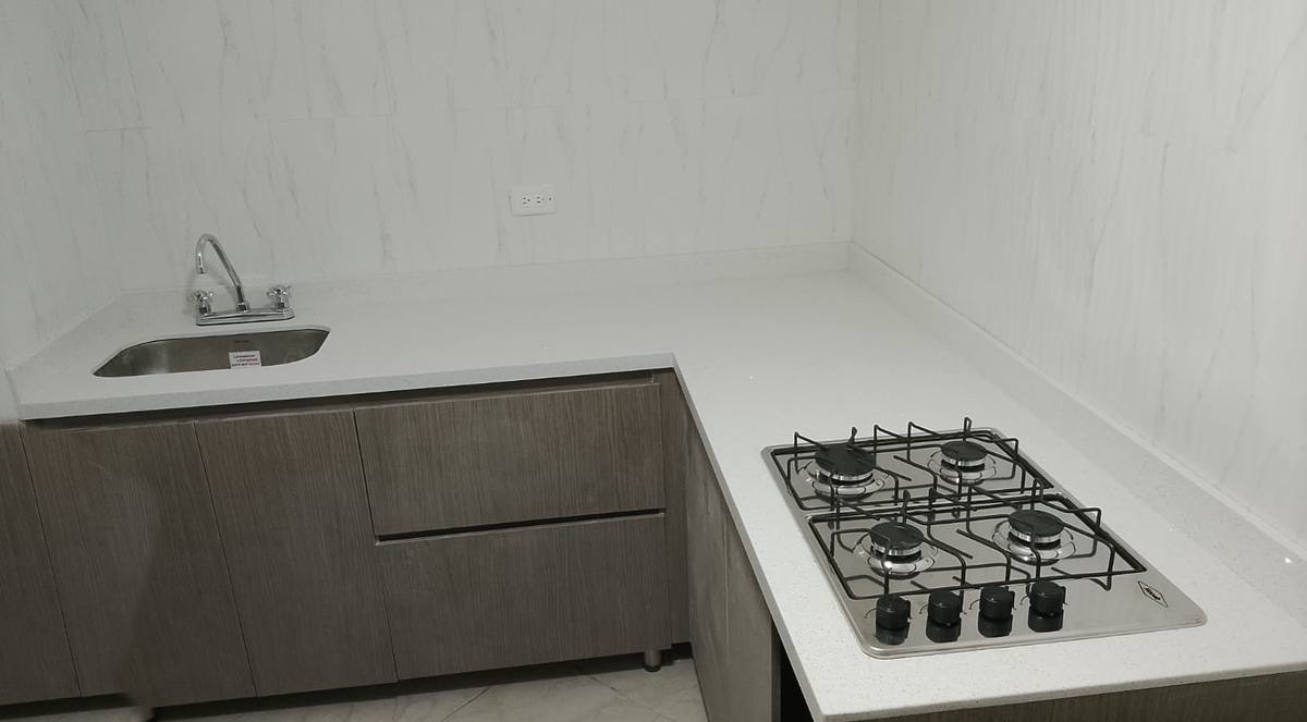 Cocina en esquina con mesón de cuarzo blanco, estufa y poceta