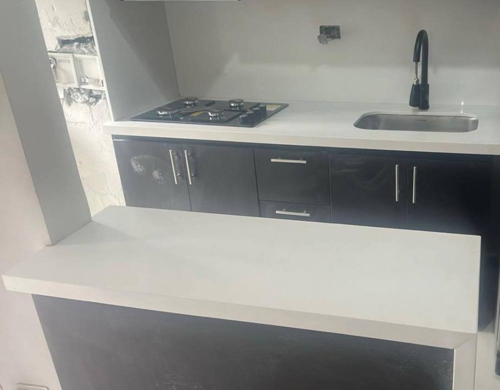 Isla de cocina en cuarzo blanco con muebles negros, estufa y poceta negra