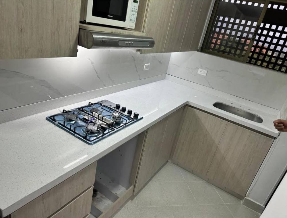 Cocina en L con mesón y salpicadero de cuarzo gris, estufa a gas y muebles de madera clara