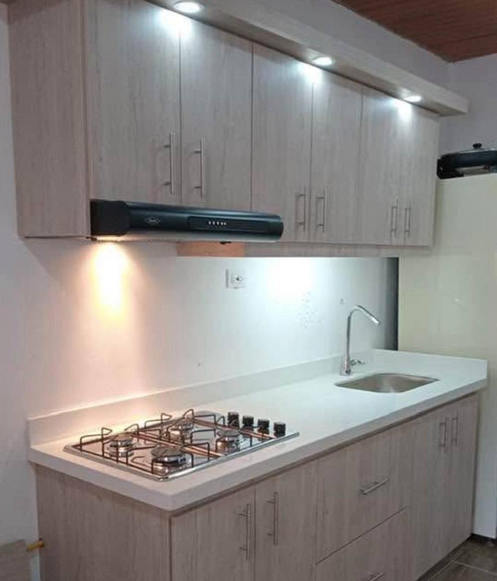 Cocina lineal con mesón de cuarzo blanco, muebles de madera clara, campana y luces led